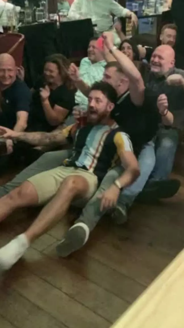 Two lines of people sat down on the floor singing a Karaoke song